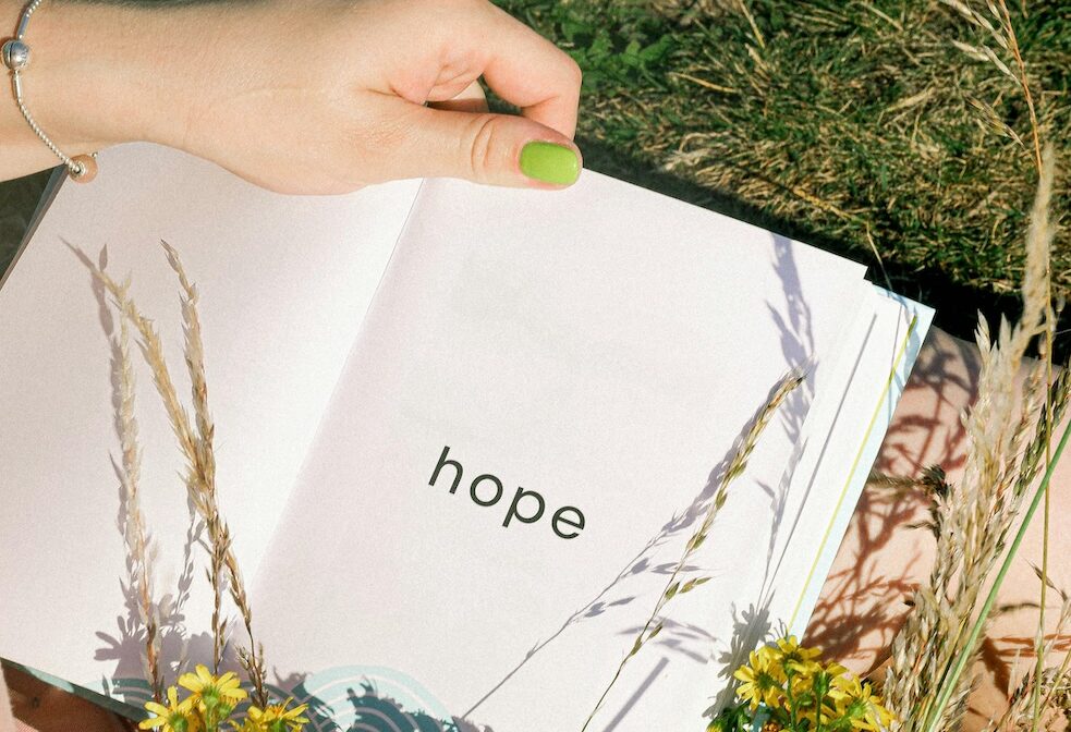 The word "Hope" typed in a journal and set in flowers on a woman's lap